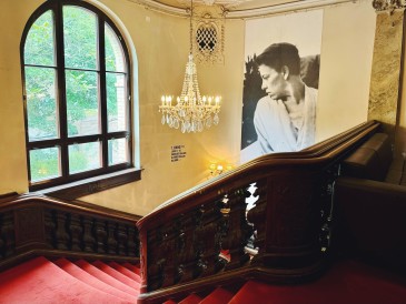 Ein Foto vom Treppenaufgang im Großen Haus des Berliner Ensembles. An der Wand ist ein großes Schwarz-Weiß-Foto von Helene Weigel, die durch das Fenster auf den Innenhof blickt.
